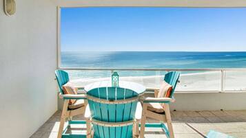 A balcony with a view of the ocean, a round table, and four chairs.