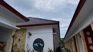 A building with a tiled roof and a circular window with a floral design. There are plants in front of the building and a patterned floor.