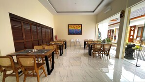 A hotel dining area with wooden tables and chairs, a fire extinguisher on the wall, and a large painting above the tables.