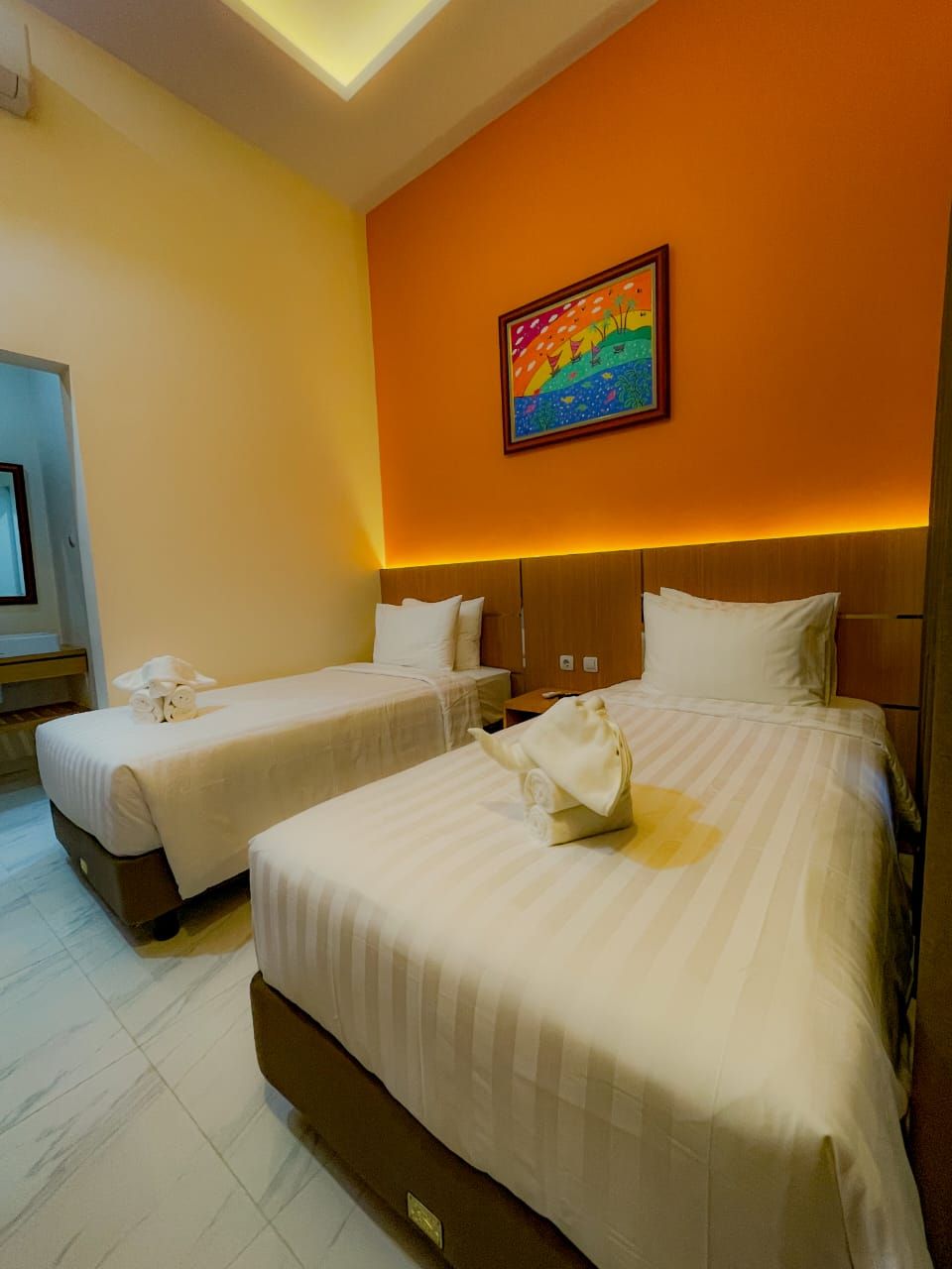 Quarto de hotel com duas camas, um quadro na parede e uma luminária no teto.