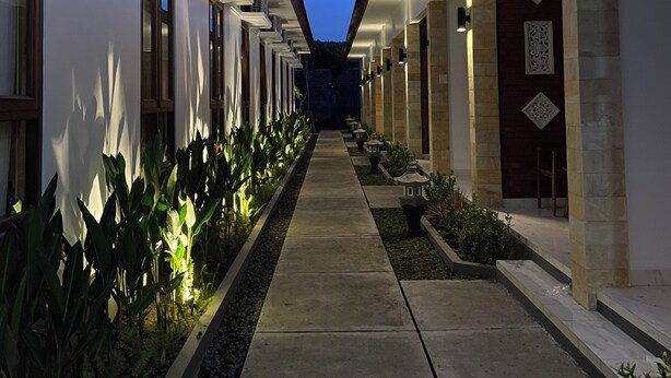 A corridor with a central walkway flanked by buildings, air conditioning units, and decorative elements.