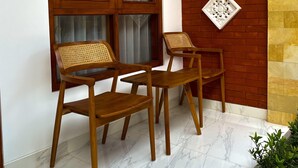 A room with a large window, two wooden chairs with woven seats, a brick wall, and decorative wall art.