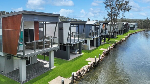 A row of modern, elevated waterfront cabins with balconies, a stone dock, and a grassy area. - Cabin 60 - Lake Conjola (Lake Conjola)