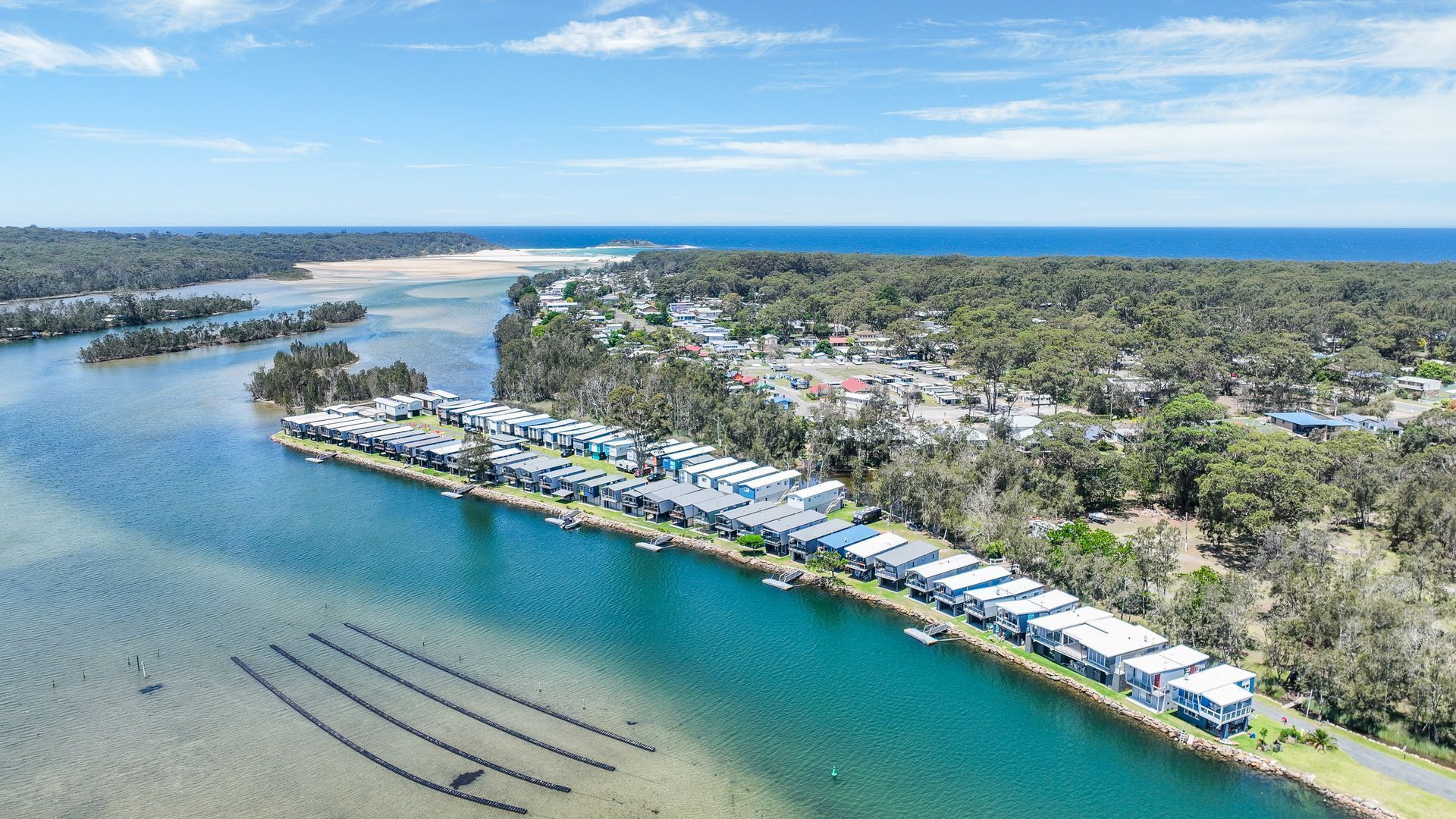 Vista aérea de un hotel costero con varias edificaciones alineadas a lo largo de la costa, conectadas por un muelle.