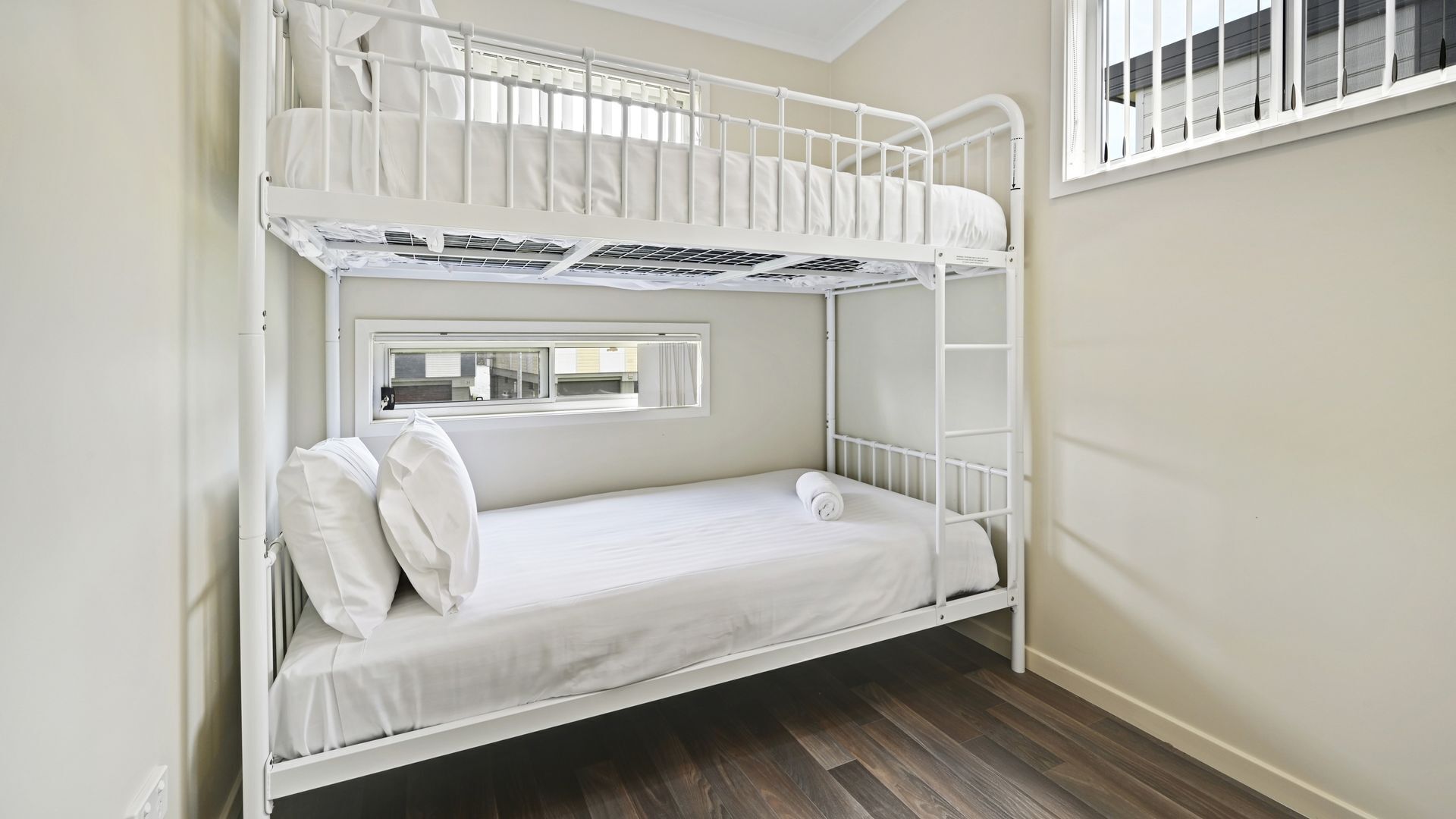 A bunk bed room with a window, white bedding, and a wooden floor.