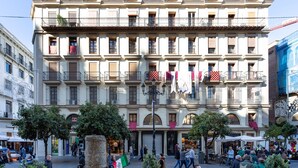 Un bâtiment historique doté de nombreux balcons, d’une entrée centrale et entouré d’arbres.
