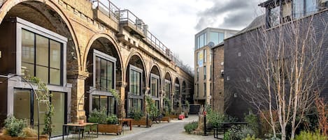 A courtyard with a brick archway, modern buildings, and outdoor seating.