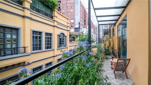 A narrow urban courtyard with yellow buildings, a glass-enclosed patio, and a chair with a bottle. - AM Manye Hotel (Kunming)