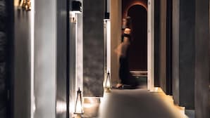 A hallway with a modern design, featuring a dark-toned door at the end, a small table with a lamp, and a wall-mounted light fixture. - AM Manye Hotel (Kunming)
