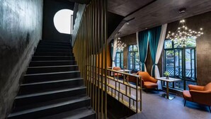 Una escalera de diseño moderno que conduce a un espacio de descanso con sillas anaranjadas y una mesa, y un gran ventanal con cortinas.