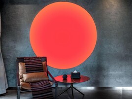 Una habitación moderna con una lámpara circular grande en la pared, un sillón de cuero y una mesita redonda con un dispensador de pañuelos.