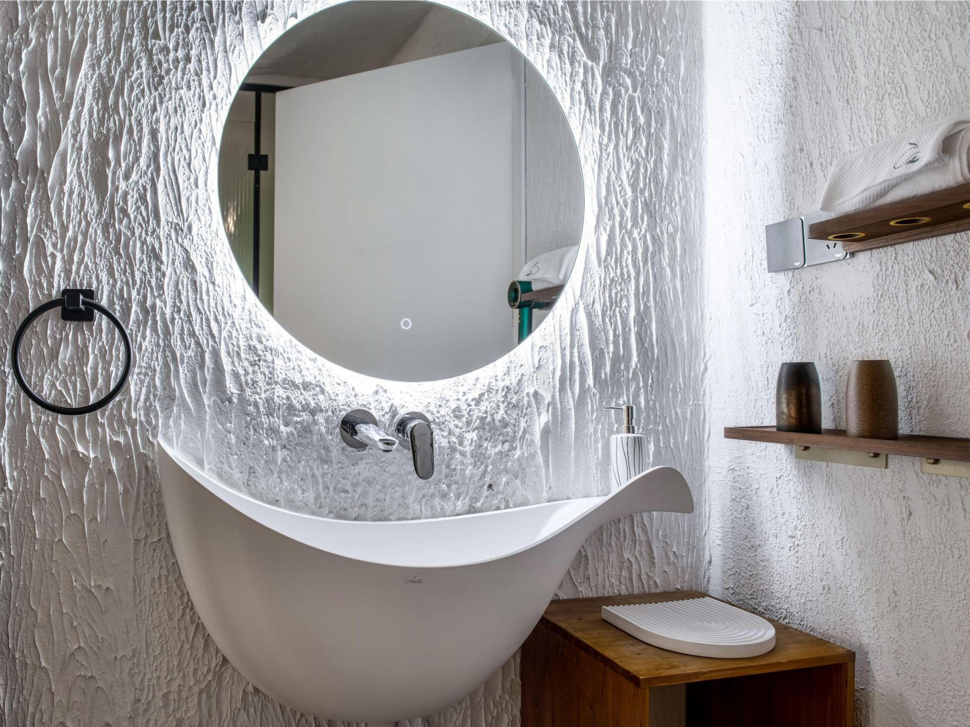 A bathroom with a unique sink design, a mirror, and a wooden shelf with toiletries.