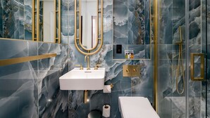 Un bagno moderno con zoccolo in marmo, accessori dorati e cabina doccia in vetro.