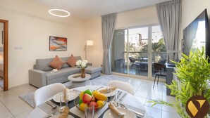Un salon moderne avec un canapé gris, une table à manger dressée pour deux personnes et un balcon offrant une vue sur la ville.