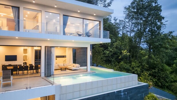 A modern two-story house with a large glass balcony, a dining area, a living room, and a swimming pool.