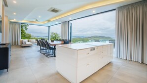 A modern kitchen with a large island, a dining area with chairs, and large windows offering a scenic view.