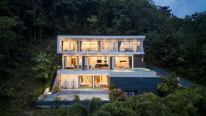 A modern two-story house with a swimming pool, surrounded by lush greenery.