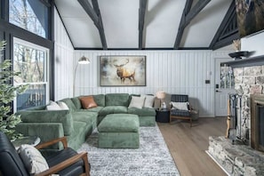 Ein gemütliches Wohnzimmer mit einem grünen Ecksofa, einem Kamin und einem großen Fenster.