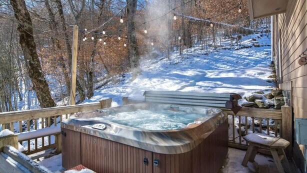 A hot tub surrounded by a wooden deck, with a snowy landscape and trees in the background. - Large, Ski-in/Ski-Out, Hot Tub, Wet Bar, Sleeps 16 (Beech Mountain)