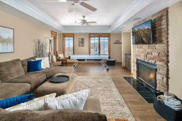 A living room with a pool table, fireplace, and large windows.