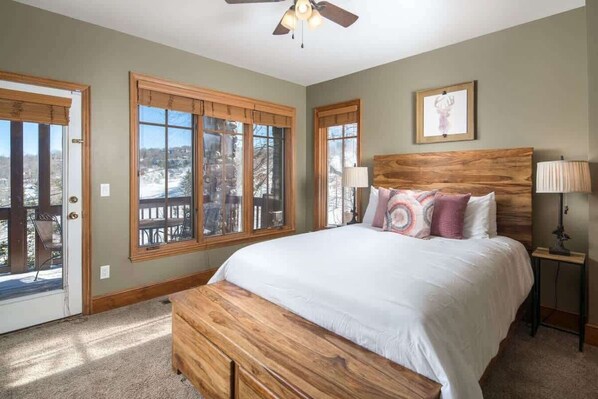 A bedroom with a bed, a ceiling fan, and large windows.