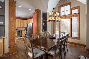 A spacious kitchen with wooden cabinets, a dining table with chairs, and a large window with a view of trees.