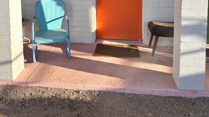 A building entrance with a white brick wall, an orange door labeled "Tequila Sunrise," a blue chair, and a small table. - Vintage Motel Room in sunny Tucson with WiFi, AC "Tequila Sunrise" (Tucson)
