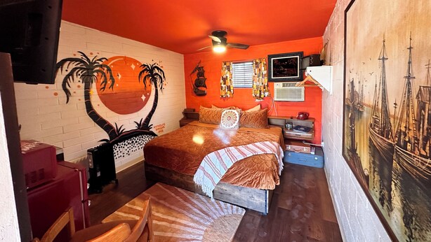 A compact bedroom with a bed, a desk, a chair, a TV, and a wall mural. - Vintage Motel Room in sunny Tucson with WiFi, AC "Tequila Sunrise" (Tucson)