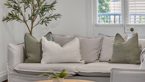 Un salon avec un canapé blanc, des coussins verts et blancs, une table basse en bois et une plante en pot.