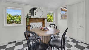 Une salle à manger avec une table ronde en bois, des chaises noires, un miroir au-dessus de la table et un sol à carreaux.