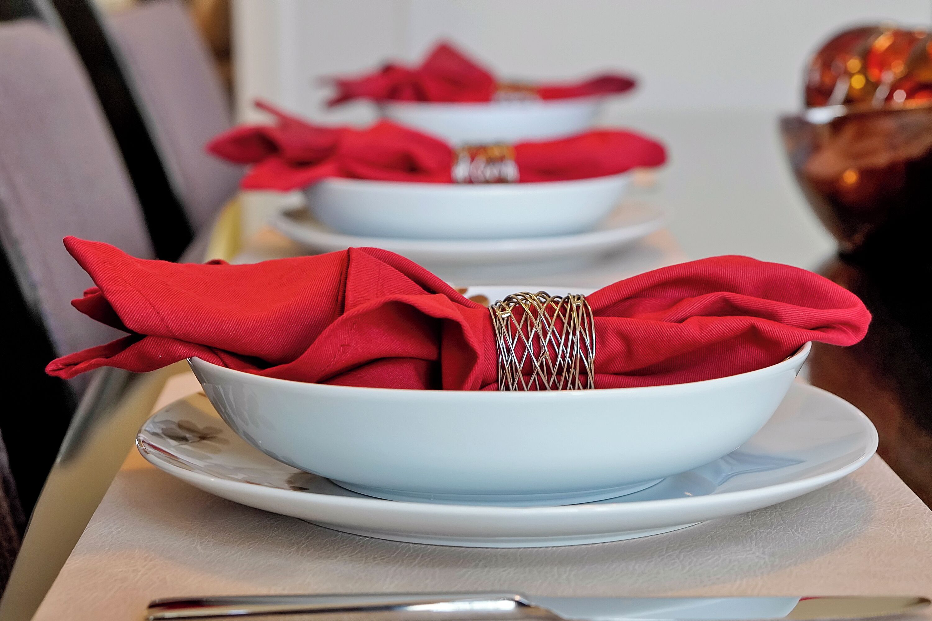 A dining table with white plates and red napkins.
