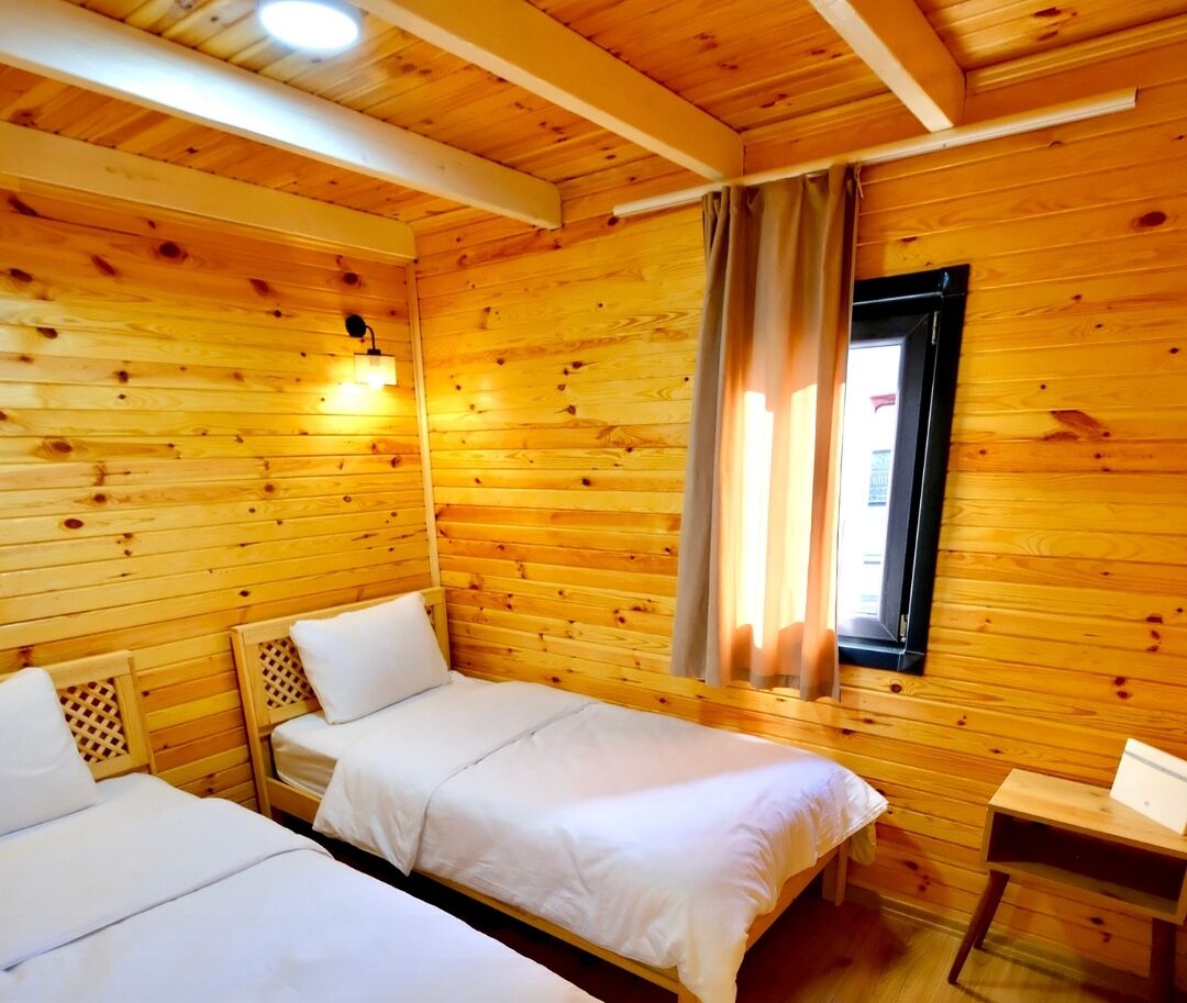 A cabin with two beds, wooden walls, a window with curtains, and a small table.