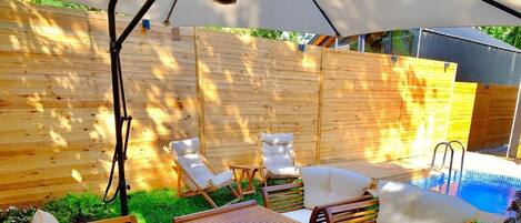 An outdoor patio with wooden furniture, a pool, and a covered area.