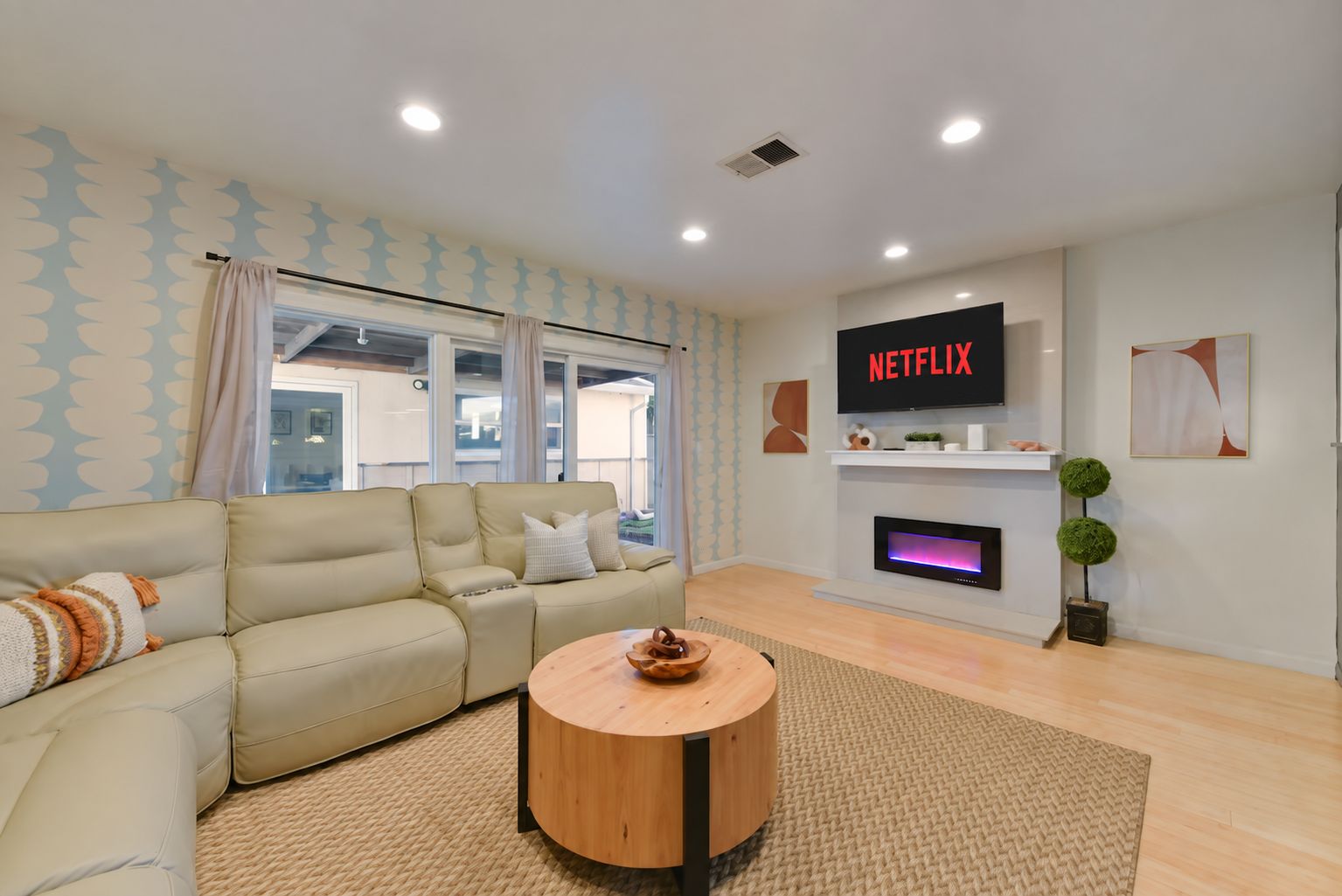 A modern living room with a sofa, a round wooden coffee table, a fireplace, and a TV mounted on the wall.
