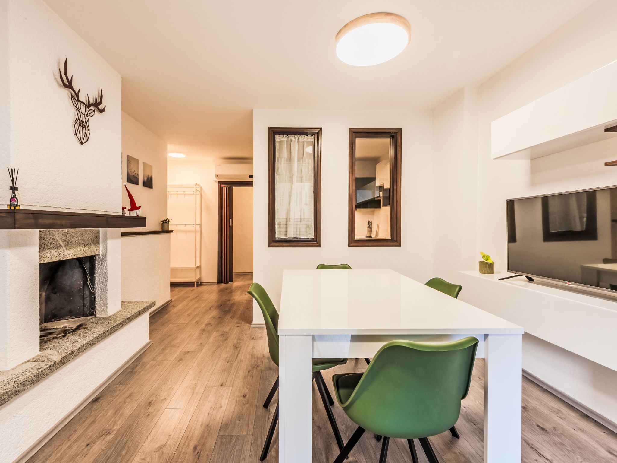 A modern kitchen with a white table, green chairs, a fireplace, and a TV.