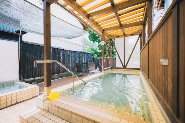 An indoor swimming pool with a wooden deck, tiled steps, and a covered area.