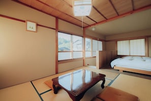 A traditional Japanese room with tatami flooring, a low wooden table, a bed with white bedding, and sliding shoji doors.