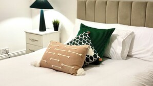 A neatly made bed with a beige headboard, white pillows, and decorative pillows with bone and leaf patterns. - Unwind at Hebburn House-Your Serene Retreat Awaits (Hebburn)