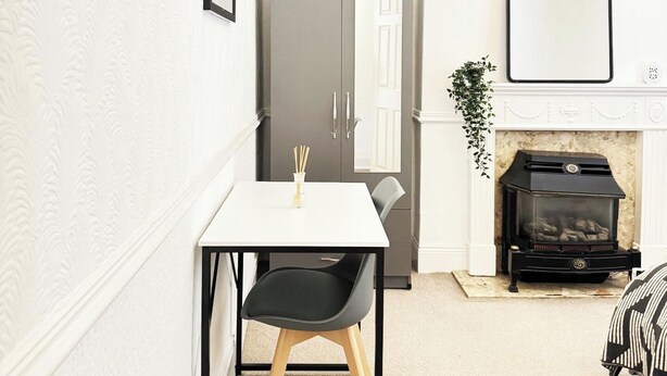 A compact living space with a dining table, a black chair, a white door, a fireplace, and a mirror on the wall. - Unwind at Hebburn House-Your Serene Retreat Awaits (Hebburn)