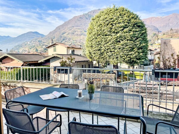 A terrace with outdoor seating, a view of a mountain, and a large tree.