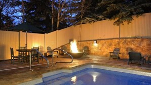 A swimming pool with a fire feature, surrounded by chairs and a covered area. - Christie Lodge Winter's Best. (Avon)