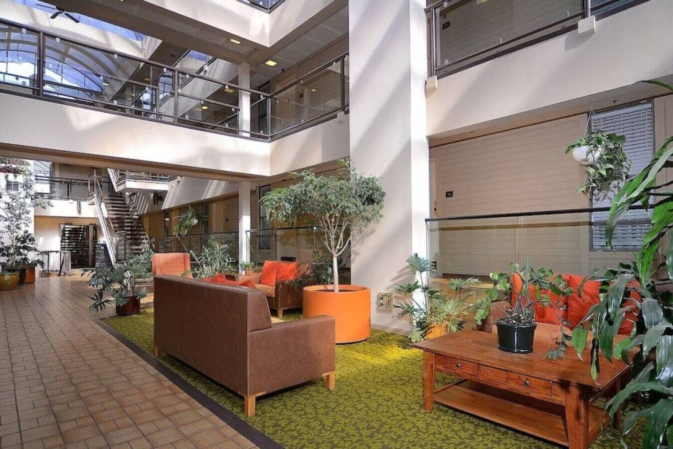 A spacious indoor area with a high ceiling, a staircase, and multiple seating areas with plants.