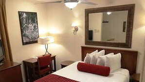A hotel room with a bed, a desk, a chair, a lamp, a mirror, and a painting on the wall. - Christie Lodge Winter's Best. (Avon)