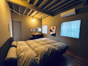 Ein Schlafzimmer mit Bett, Schreibtisch, Stuhl, Fenster und Deckenbalken.