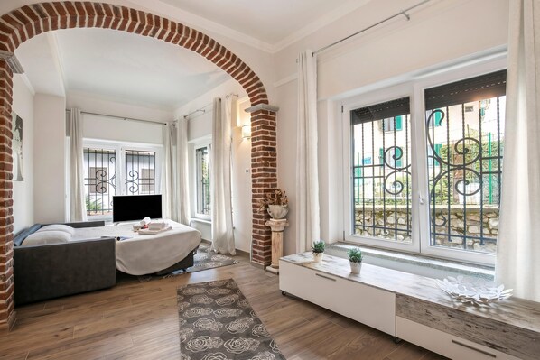 Ein modernes Zimmer mit einem Bett, einem Fernseher, einem Fenster mit Metallgitter und einem Ziegelbogen.