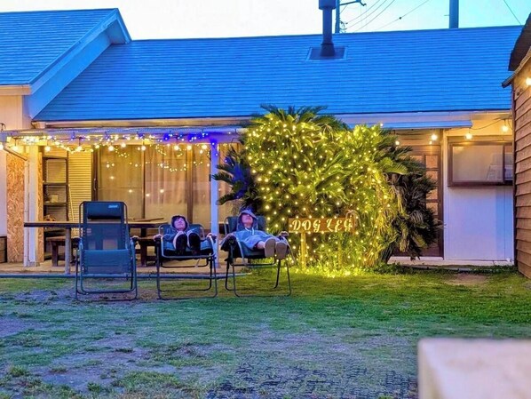 A house with a covered outdoor seating area, a small tree decorated with lights, and a sign that reads 'DOG LEG.'