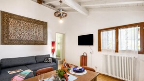 Una sala de estar con un sofá, una mesa de comedor con platos y vasos, un televisor montado en la pared y un radiador.
