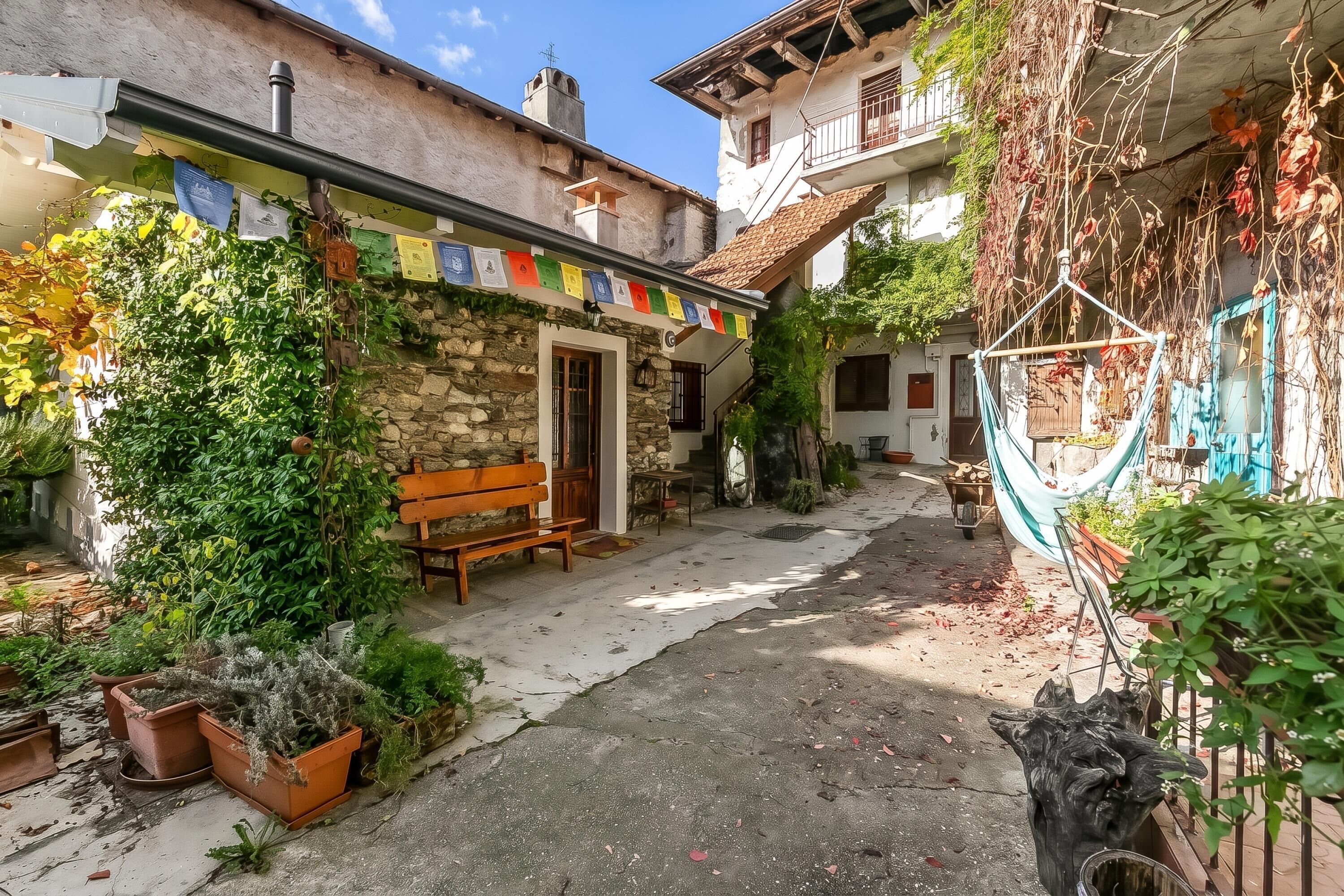 Un patio con muro de piedra, banca de madera y plantas en macetas.