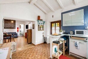 A spacious living area with a wooden floor, a dining table, a sofa, and a kitchen area with a microwave and a kettle.