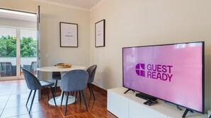 Ein modernes Zimmer mit Essbereich, einem großen Flachbildfernseher, der „GUEST READY“ anzeigt, und gerahmten Bildern an der Wand.